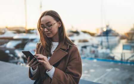 Young woman calling mobile phone in europe city. Girl in glasses using smartphone technologyの写真素材