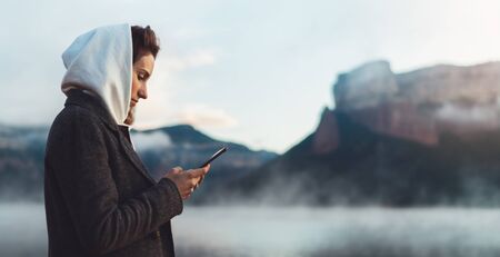 hipster tourist using smartphone planning trip on foggy lake, mist in mountain nature, traveler girl hold mobile phone, enjoy wifi internet, lifestyle holidayの写真素材