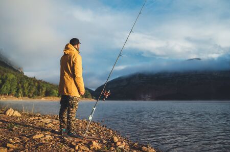 fishery concept, fisherman enjoy hobby with fishing rod on evening lake, person catch fish on background blue sky, holiday relaxation vacationの写真素材