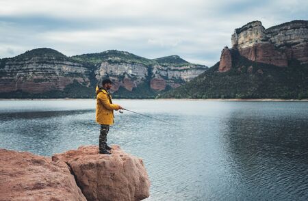 fishery concept, fisherman hold fishing rod, man enjoy hobby sport on lake, person catch fish on river on background mount, holiday relaxation vacationの写真素材