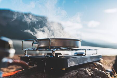 camping cooking in nature outdoor, vapours crop, prepare breakfast picnic in mist morning; cooker food metal gas stove on stone; campsite lifestyle, hot food hiking tripの写真素材