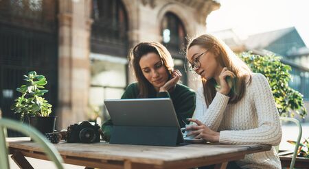 Girls drink coffee relax in cafe outdoor in europe city. Freelancer communicate on project, woman shopping online on wifi tablet. Working business processの写真素材