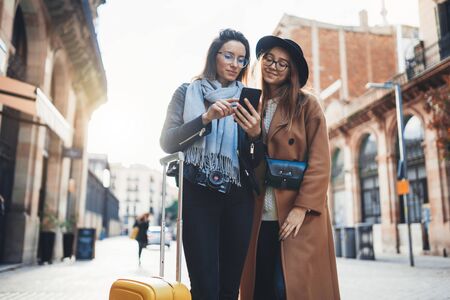 Girls plans trip on internet mobile phone, tourist using smartphone, hipster travels in europe city. Holiday friendship concept. Travelers hold cellphoneの写真素材