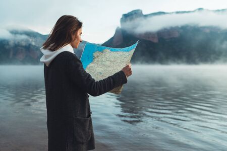 hipster tourist planning trip on foggy lake, mist in mountain nature, traveler girl look map, landscape vacation trip, enjoy lifestyle holiday conceptの写真素材