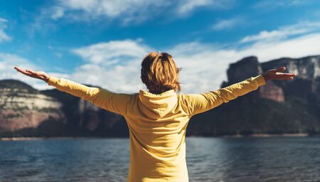happy tourist traveler standing with raised hands, back view girl hiker enjoying mountains lake with arms outstretched breathing of fresh clean air in trip in spain, relax holidayの写真素材