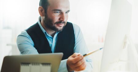 bearded businessman looking in monitor computer at home workplace. man working at house social distance, finance consultant online communication work process, online educationの写真素材