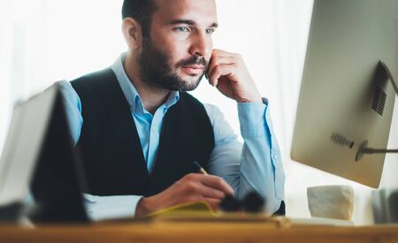 bearded businessman looking in monitor computer, freelancer online communication work process at home workplace, man working at social distance, online educationの写真素材