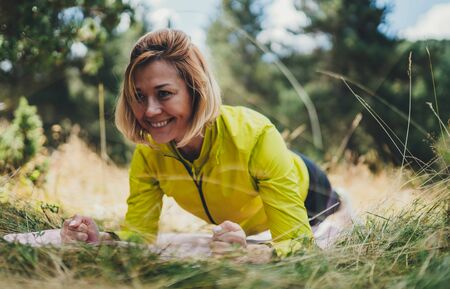 Fit girl doing plank exercise outdoor in park warm summer day, activity with stretch legs. Smile...