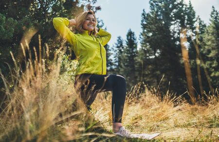 Fun girl exercising outdoors in sun summer day, activity with stretch legs in park. Smile fitness woman stretching exercises training outside. Sportswoman isolaition in nature. Healthy lifestyle conceptの写真素材