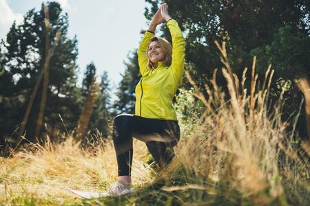 Fun girl exercising outdoors in sun summer day, activity with stretcharms and  legs in park. Smile woman stretching exercises training outside. Sportswoman isolaition in nature. Healthy lifestyleの写真素材