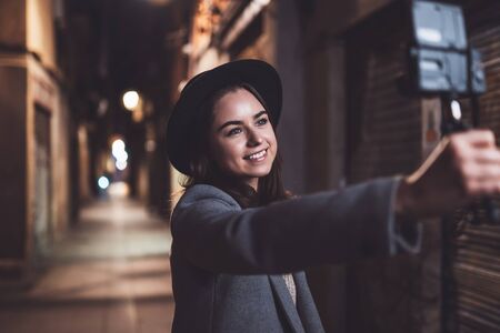 Traveler female blogger shooting video for vlog social media with digital camera. Smiling woman vlogger taking selfie video on light night cityの写真素材