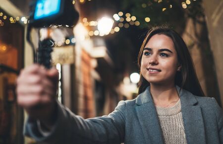 Traveler female blogger shooting video for vlog social media with digital camera. Young woman vlogger taking photo selfie on background light night city illuminationsの写真素材