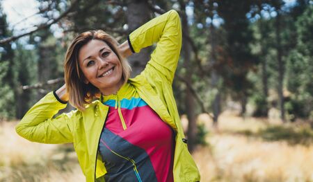 Smile girl exercising outdoors in green park, activity with stretch arms. Young fitness woman doing stretching exercises training outside. Sportswoman in nature. Concept of healthy lifestyleの写真素材