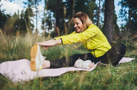 Smile girl exercising outdoors in green park, activity with stretch legs. Young fitness woman doing stretching exercises training outside in nature. Healthy lifestyle conceptの写真素材
