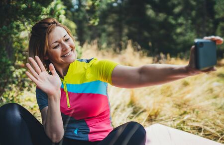 Young smile woman video calling on internet for vlog social media with mobile phone showing hi. Isolation girl laughing using smartphone after training in park. Tourist video communication on cellphone after exercising sport outdoorsの写真素材
