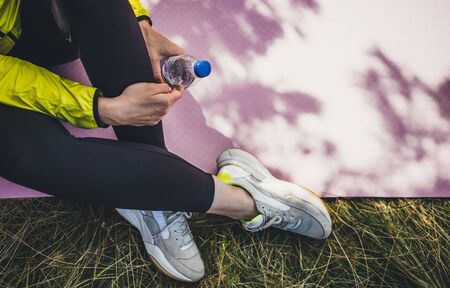 Top view girl  with bottle of water relax after exercising outdoors on yoga mat, isolation fitness woman in sneaker stretch training outside on green grass. Empty space for your text. Healthy lifestyle conceptの写真素材