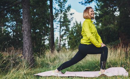Smile girl exercising outdoors in green park, activity with stretch legs. Young fitness woman doing stretching exercises training outside. Healthy lifestyle conceptの写真素材