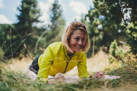 Fit girl doing plank exercise outdoor in park warm summer day, activity with stretch legs. Smile sportswoman  training isolaition in nature. Healthy lifestyleの写真素材