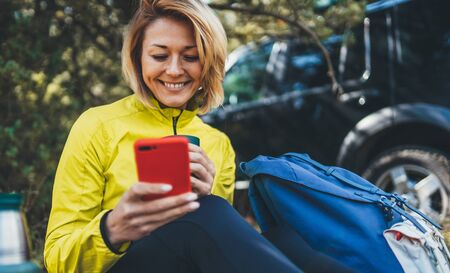 Happy joy tourist with backpack communication on cellphone while traveling auto. Young woman smiles showing teeth calling on mobile phone summer green forest. Isolation girl laughs using smartphone have fun emotion outdoorsの写真素材