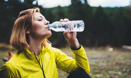 Girl quenches thirst after fitness, person drinking water from plastic bottles relax after exercising sport outdoors, woman isolation training in park, healthy lifestyle concept, sportwoman drink water after joggingの写真素材