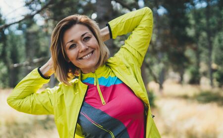Sport woman smiling  in nature, Relaxing activity with stretch arms. Young fit woman doing stretching exercises training outside in green park. Concept of healthy lifestyle. Girl exercising outdoorsの写真素材