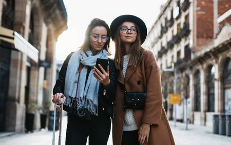 Girls plans trip on internet mobile phone, tourist using smartphone, travels in europe city. Holiday friendship concept. Travelers hold cellphone, online technologyの写真素材