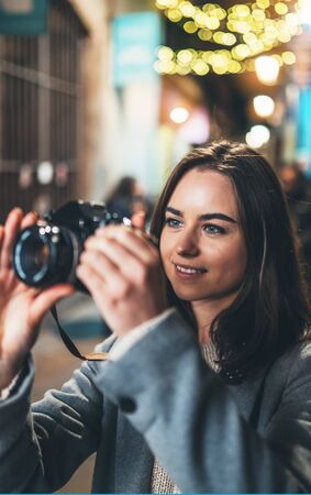 Photographer young girl with retro camera take photo on background bokeh light in night city,  photo hobbyの写真素材