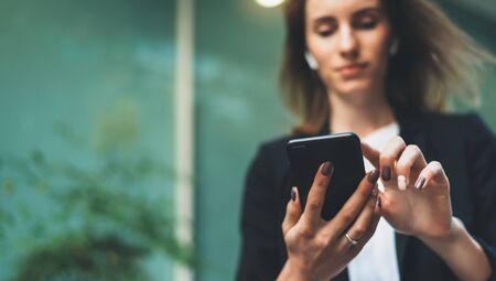Close-up image of young hipster girl using modern smartphone device near office, female hands typing text message via cellphone, social networking conceptの写真素材