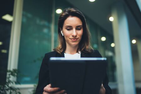 portrait professional female banker standing near office in evening street communicates online by tablet. Businesswoman pushing message to colleagues using computer  on background neon lightsの写真素材