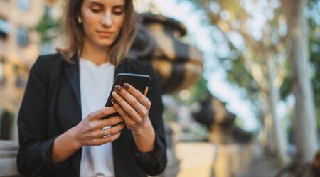 Close up woman hand hold using smart phone on outdoor park street n warm summer day,  female listening to music in earphones searching information on cell telephoneの写真素材