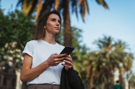 pretty young girl walks through the Park after office work and chats in messengers with colleagues manager using Internet device cellphoneの写真素材