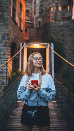tourist girl blonde with glasses and camera using mobile phone  traveling evening old historical...