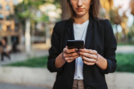 Successful woman walking outside in city park  hold in hand mobile phone chatting with friends, businesswoman typing on touch screen of cellphone while internet technology outdoorsの写真素材