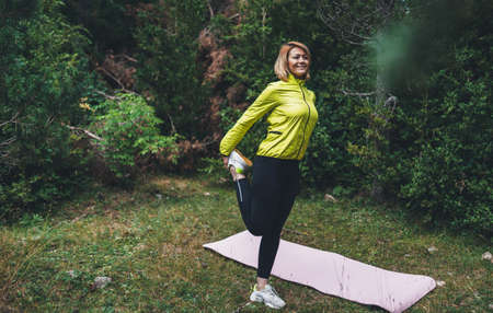 Smile girl exercising outdoors in green park, activity with stretch legs. Young fitness woman stretching exercises training outside. Sportswoman isolaiton in nature. Healthy lifestyle conceptの写真素材