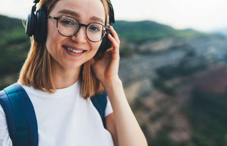 portpait smiling young woman traveler with backpack and hipster glasses listening to favorite music...