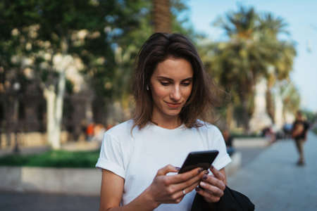 Beautiful young stylish woman walking  streets using modern smartpone, hipster female blogger typing text message on her cellphone in parkの写真素材