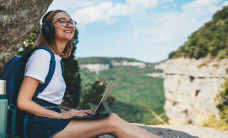 happy girl enjoys freedom in mountains listening to music on headphones and communication on digital tablet, traveler woman planning hiking walk in laptop looks at an online map outdoorsの写真素材