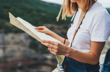 tourist girl holding in hands map resting during summer vacation on background green mountains landscape, traveler woman plans route leisure in nature outsideの写真素材