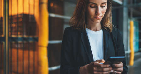 successful businesswoman hold in hands smartphone during a lunch break outside office, Manager uses mobile phone in city outdoors, cute girl in suit writes message on cellphone, empty spaceの写真素材