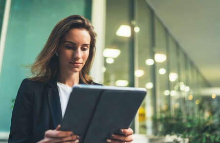 Modern businesswoman. Beautiful young woman holding digital tablet and looking on screen touch pad...