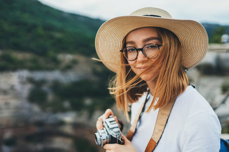 portrait blonde tourist girl in hat uses retro camera walking in mountain nature outdoor, young...
