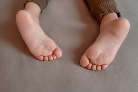 Bare childrens feet stick out from under the blanket. Warm and cozy photo in a dark key. To wallow and rest in bed on a cloudy day. The child plays in bed.の写真素材