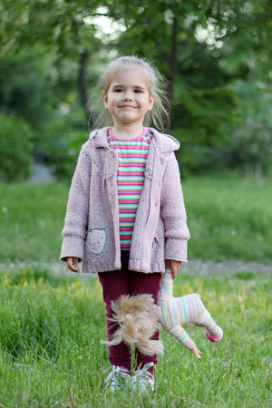 Stylish little girl standing in the park with toy doll in her hand, spring, vacation, outdoor portraitの写真素材