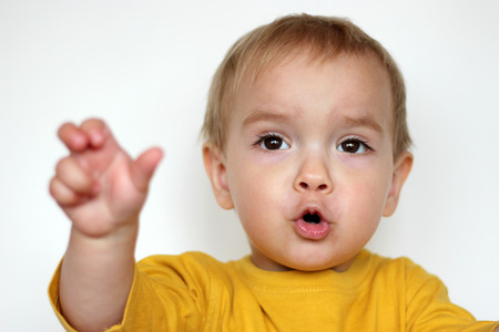 Handsome rapturous small toddler boy in yellow T-shirt with face like he is singing a song with enthusiasm over white background, face emotions concept, indoor close-upの写真素材