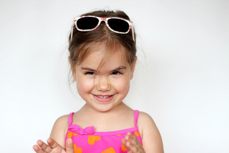 Cute happy baby girl wearing swimming suit, sun glasses over white background, summer vacation...
