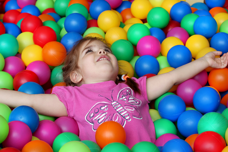 Happy girl playing and having fun at kindergarten with colorful balls, family weekend concept, happy birthday and merry partyの写真素材