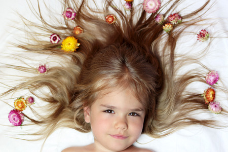 Cute small girl lying on her long light brown hair laying down having a creative hairstyle with bright flowers, beauty and health concept, indoor portraitの写真素材