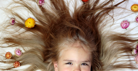 Cute small girl lying on her long light brown hair laying down having a creative hairstyle with bright flowers, beauty and health concept, indoor portraitの写真素材