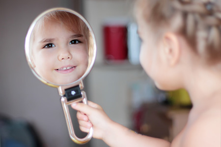 Lovely little girl smiling to her reflection in a round mirror, closeup portraitの写真素材