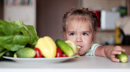 Cute little girl preparing vegetable salad and playing with pepper, healthy food concept, indoor portraitの写真素材